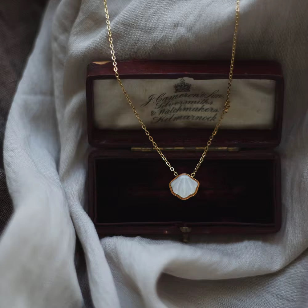 Gold necklace with a white pendant in an open jewelry box on a white fabric background