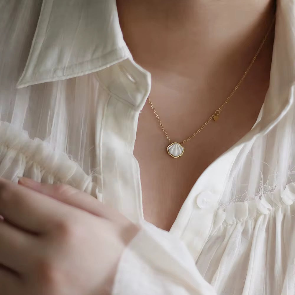 Close-up of a person wearing a delicate gold necklace with a heart pendant, against a blurred background.