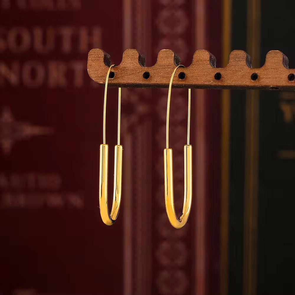 Gold earrings hanging on a wooden earring stand with a blurred background