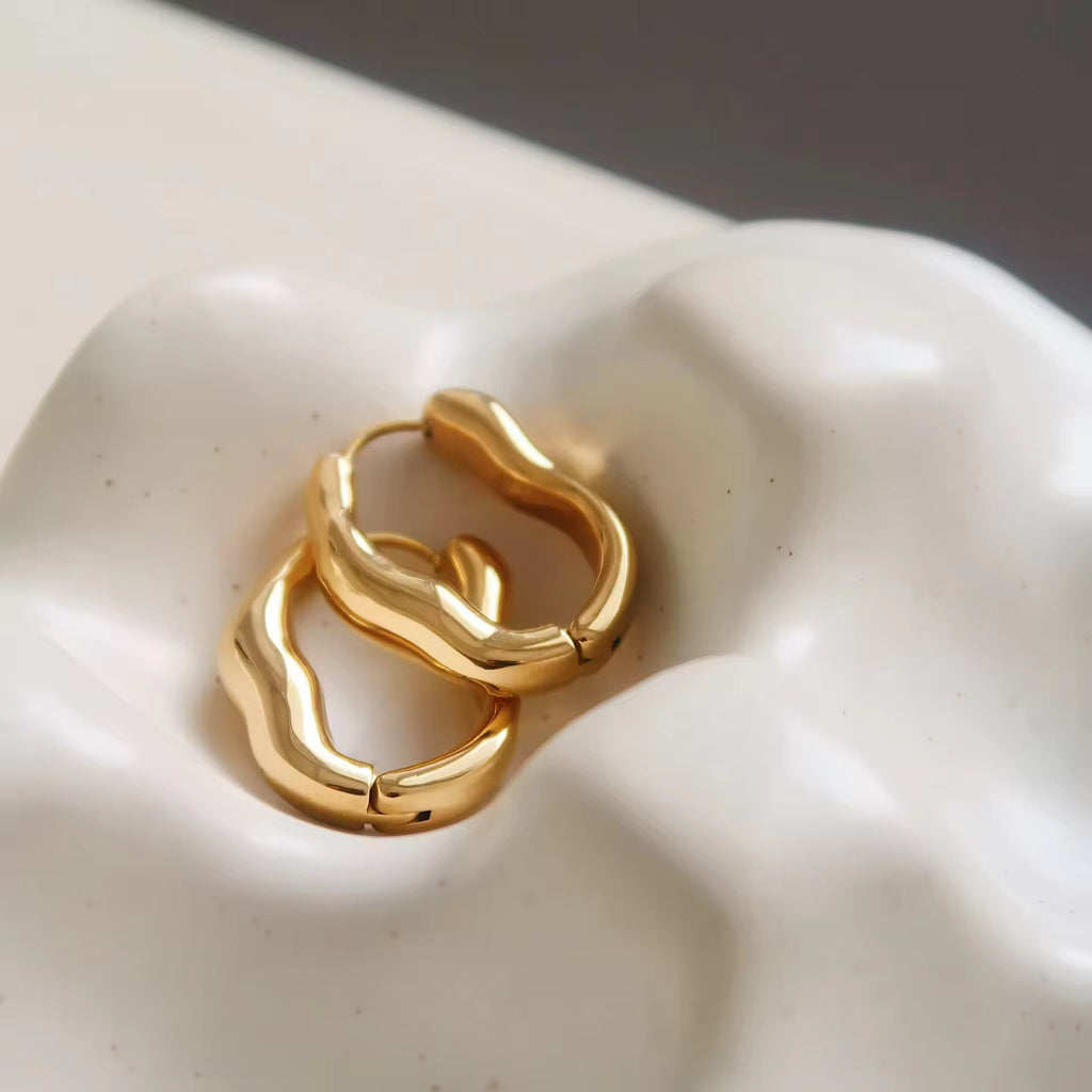 Gold hoop earrings on a white ceramic dish. 18K Gold Plated Stainless Steel, preimum, high quality, hypoallergenic, irregular gold hoop. 