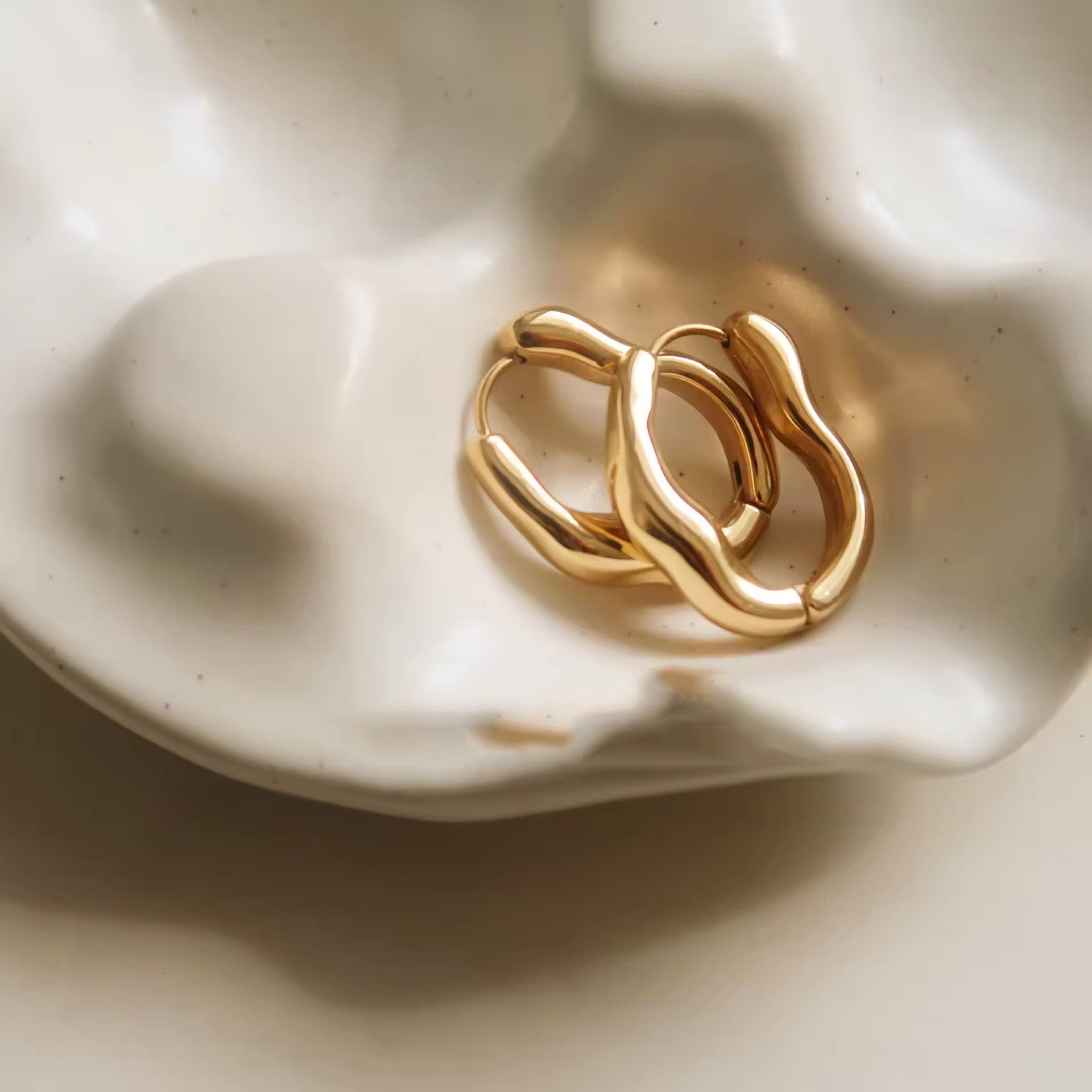 Gold hoop earrings on a white ceramic dish