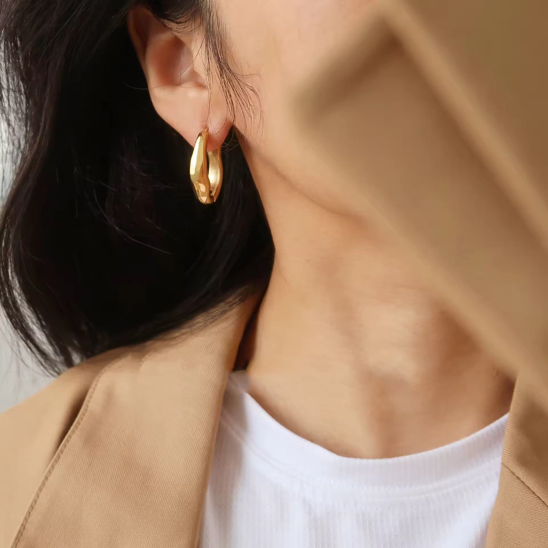 Close-up of a person wearing gold hoop earrings with a neutral background