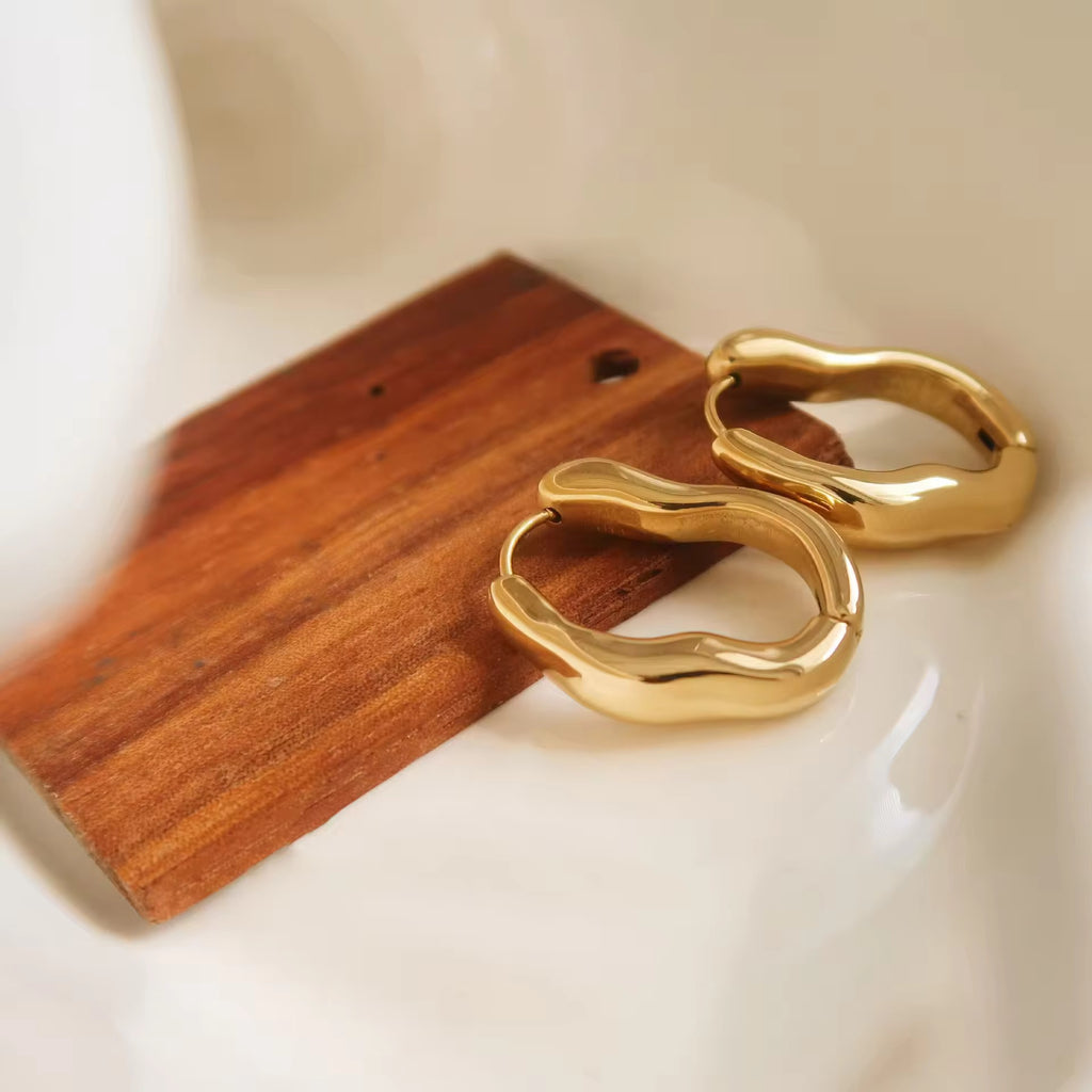 Gold hoop earrings on a wooden block with a neutral background