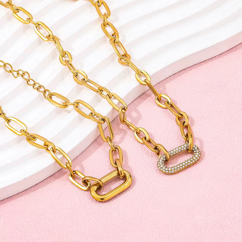 Gold chain necklace with a heart-shaped clasp on a pink and white background