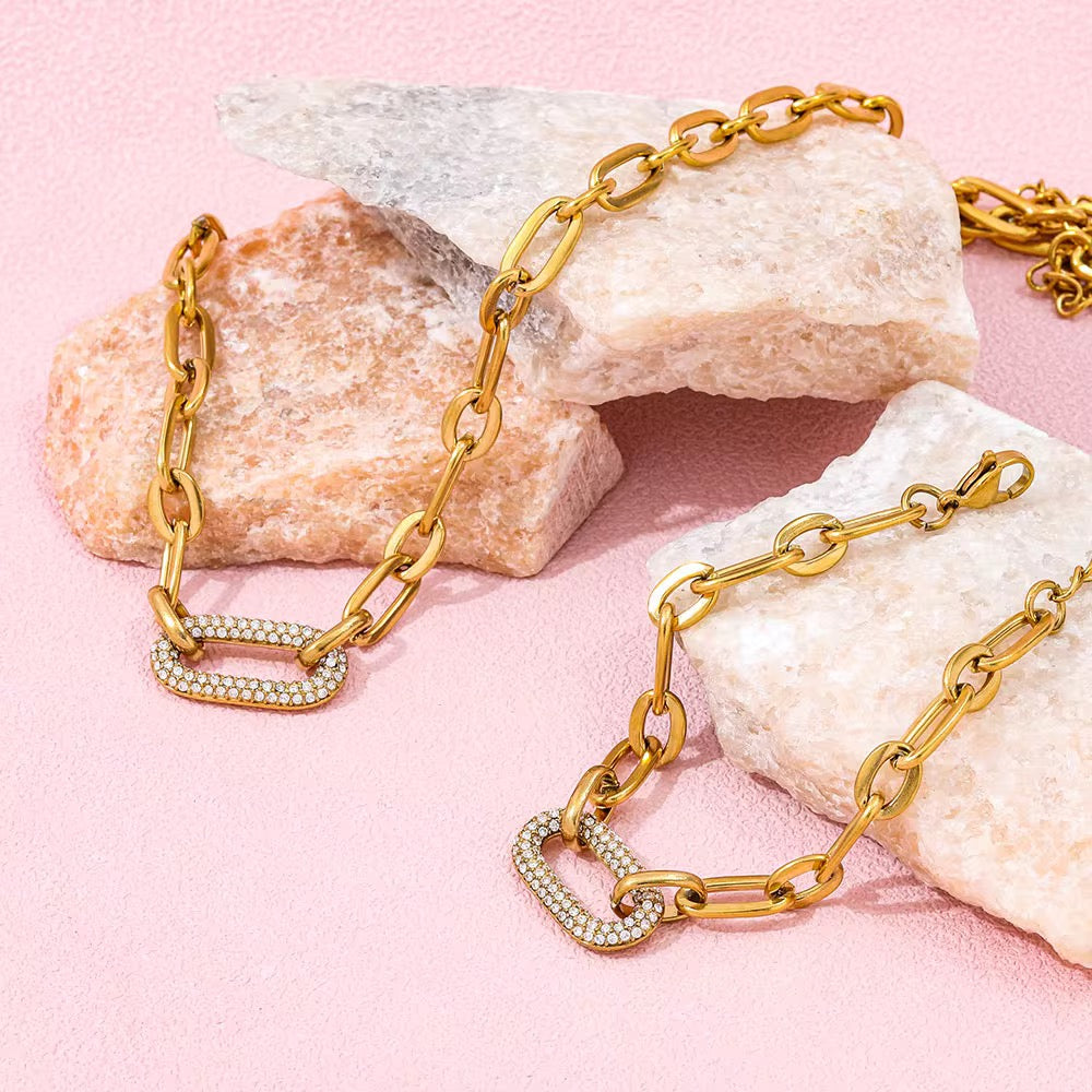 Gold chain necklace with diamond accents on a pink background