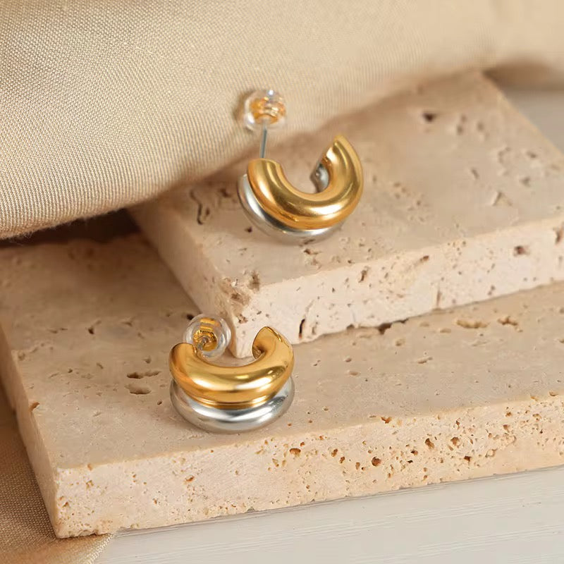 Gold and silver earrings on a textured beige surface