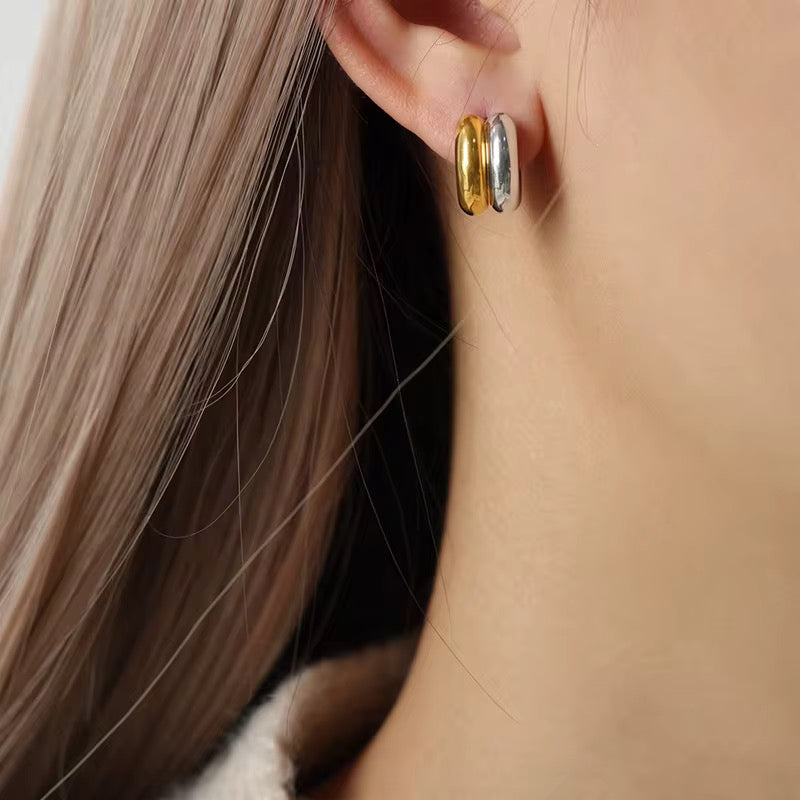 Close-up of a person wearing two-tone hoop earrings with blonde hair.