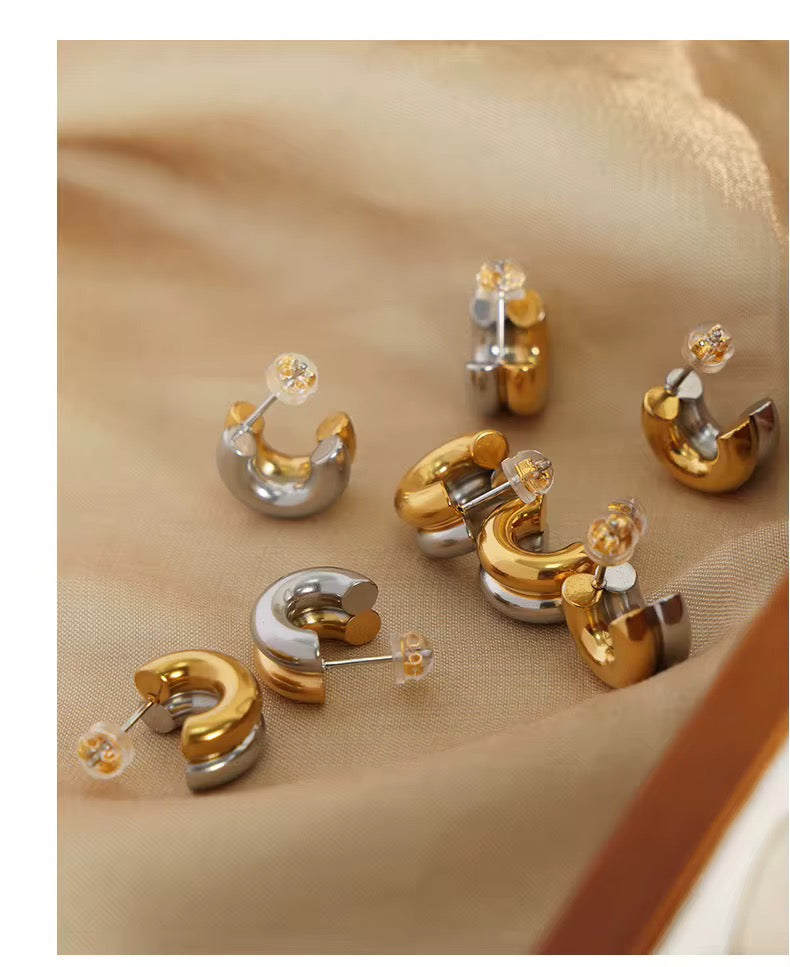 Pair of gold and silver hoop earrings on a beige fabric background