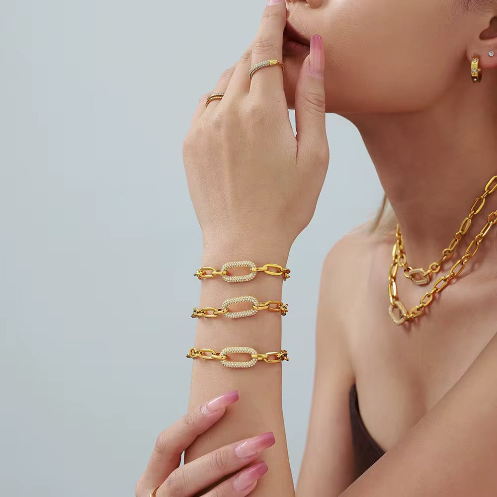 Gold jewelry set including bracelet, necklace, and ring on a neutral background