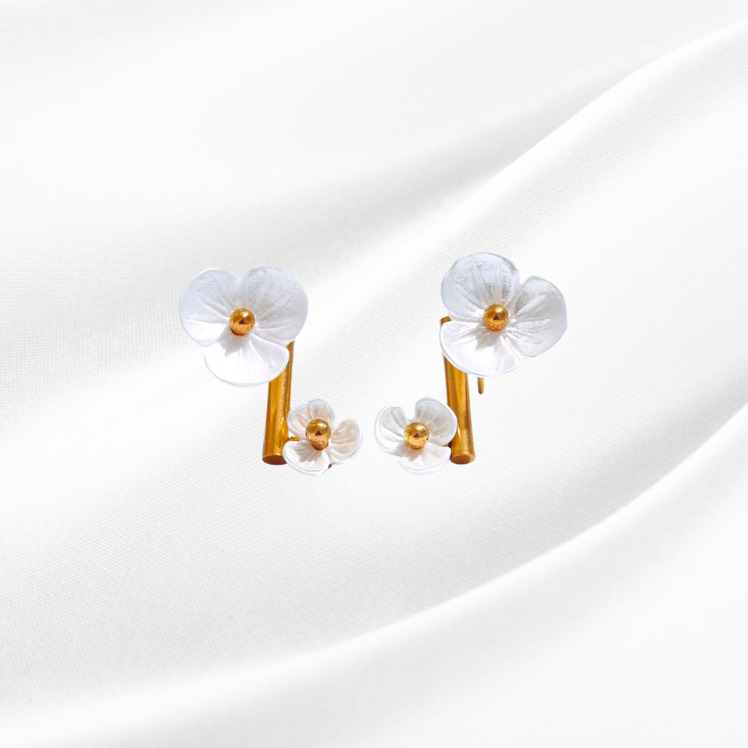 Pair of white flower-shaped earrings with gold centers on a light gray background