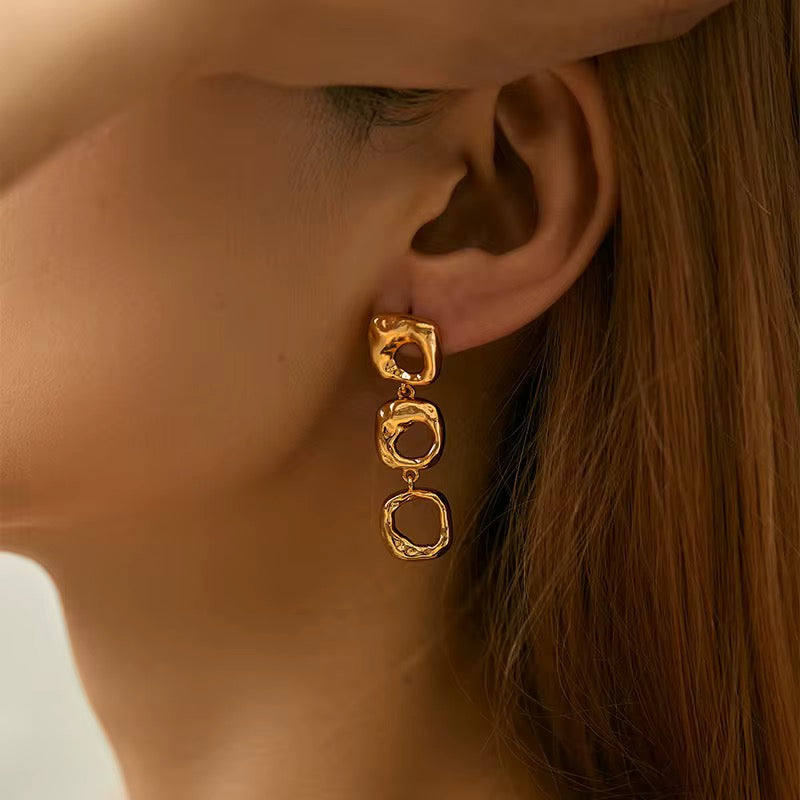 Gold earrings worn by a person with a neutral background