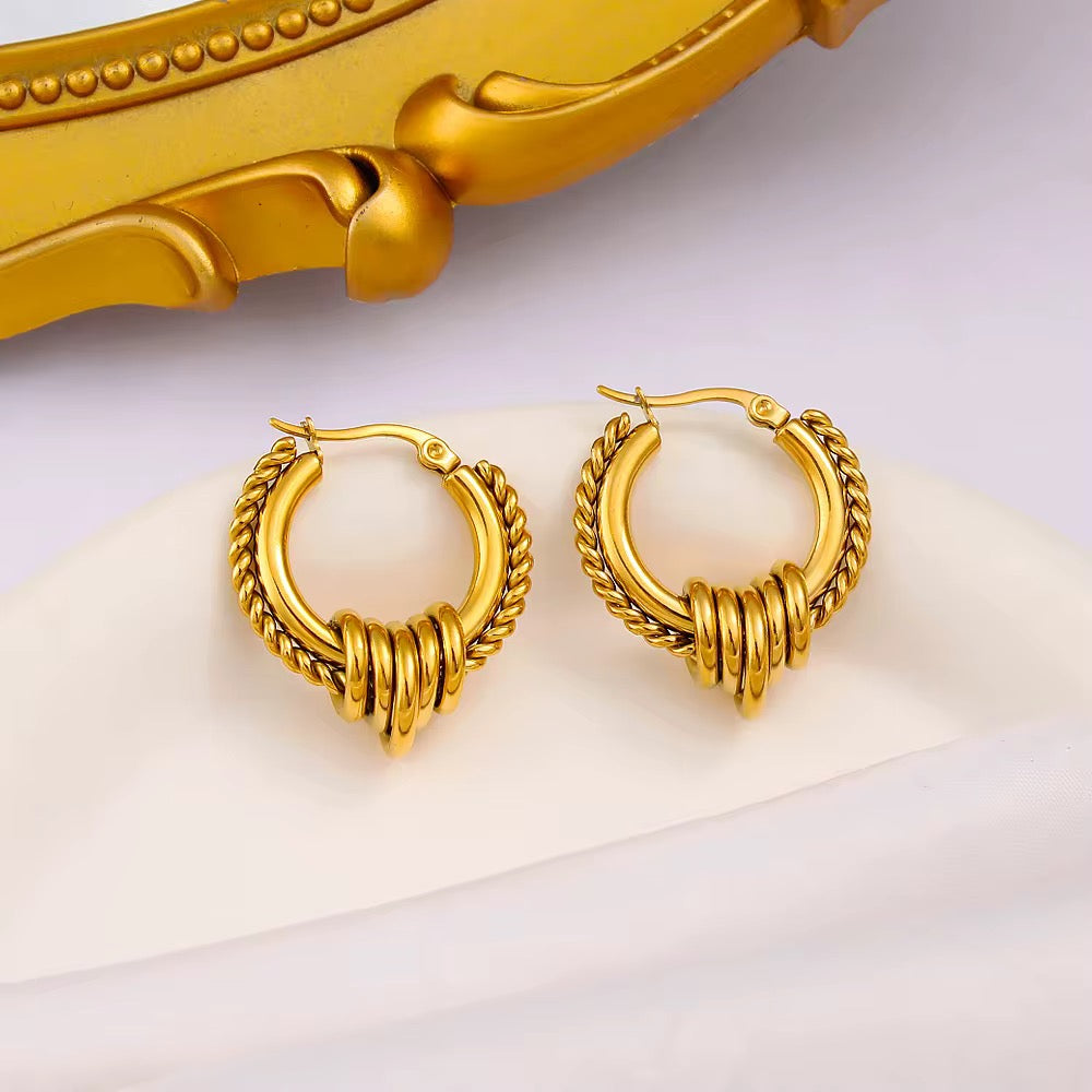 Gold hoop earrings on a white surface with a decorative gold frame in the background