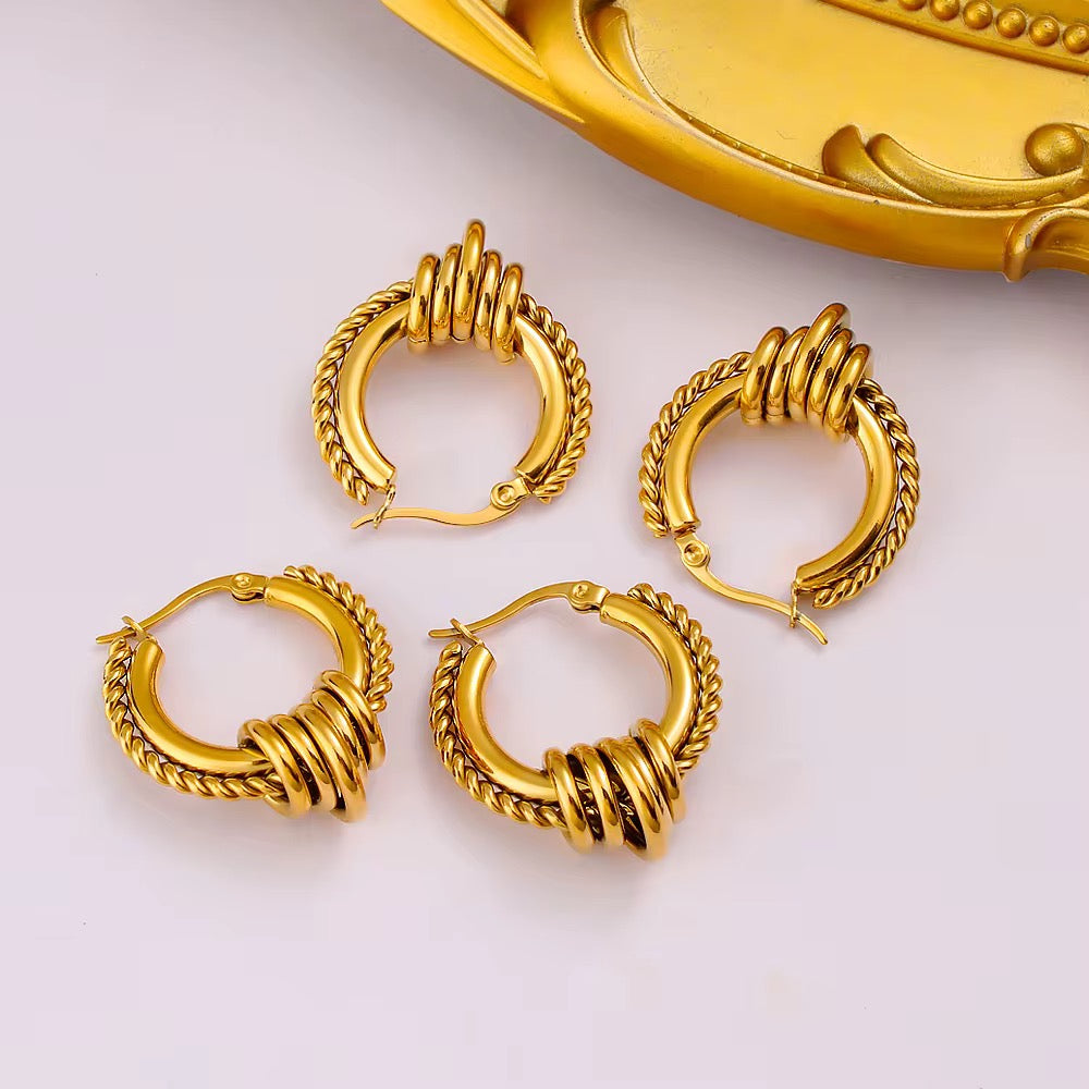 Set of gold hoop earrings on a white background with a decorative gold object.