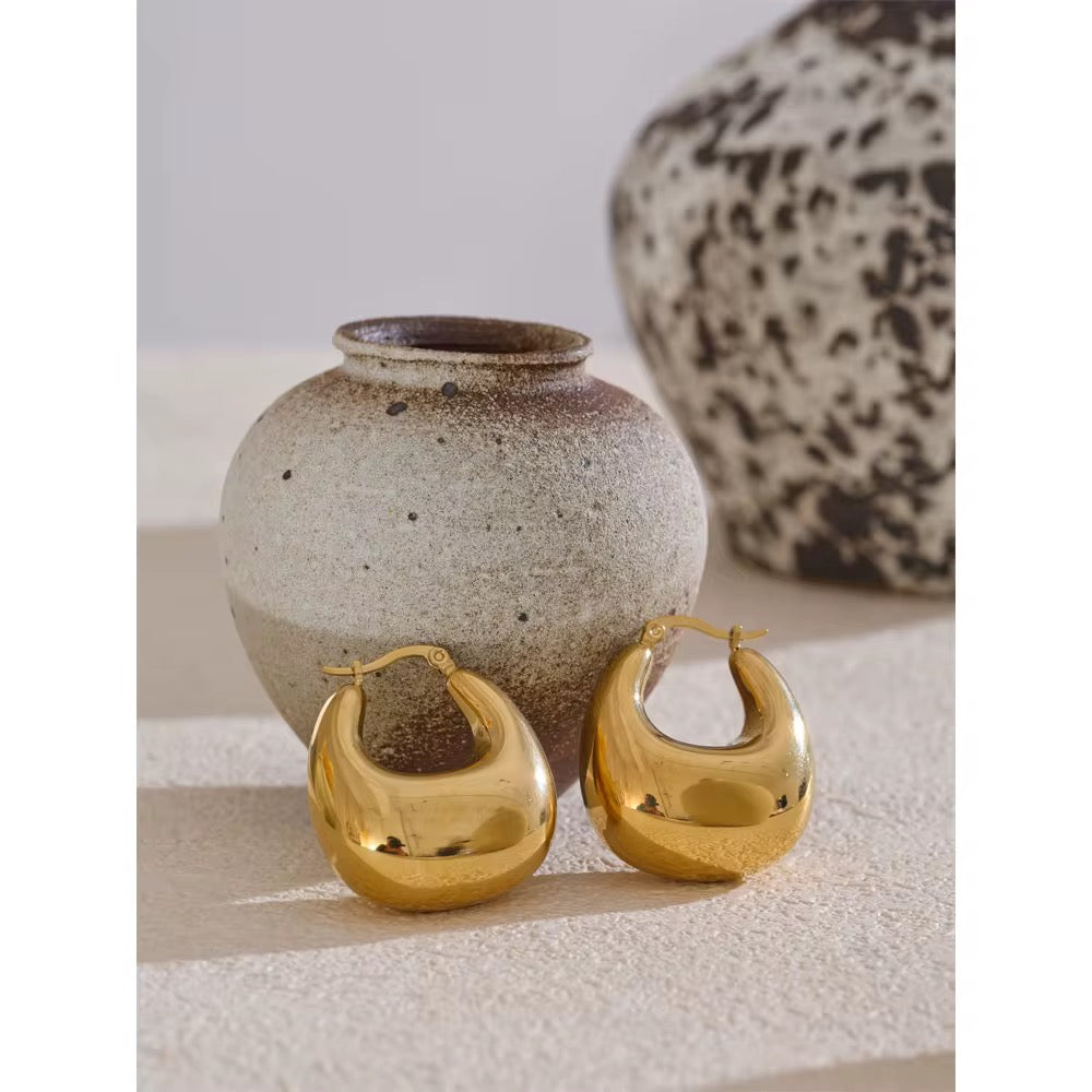 Gold earrings and a ceramic vase on a textured surface