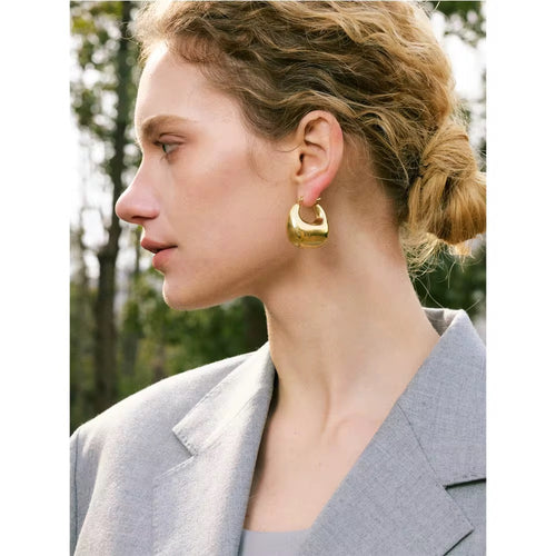 Woman wearing gold hoop earrings with a blurred natural background