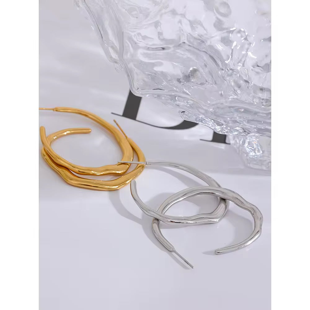 Gold and silver snake-shaped earrings on a textured white surface.