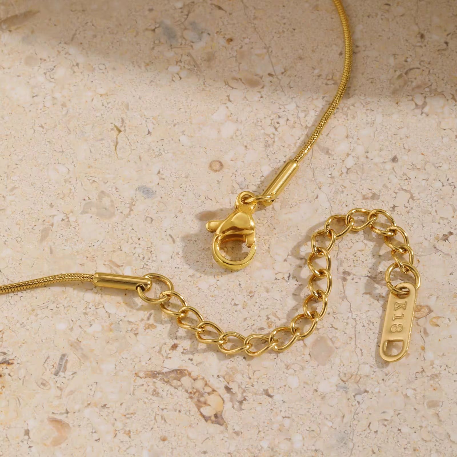 Gold chain bracelet with clasp on a beige stone surface