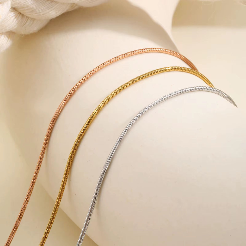 Three gold necklaces on a beige surface