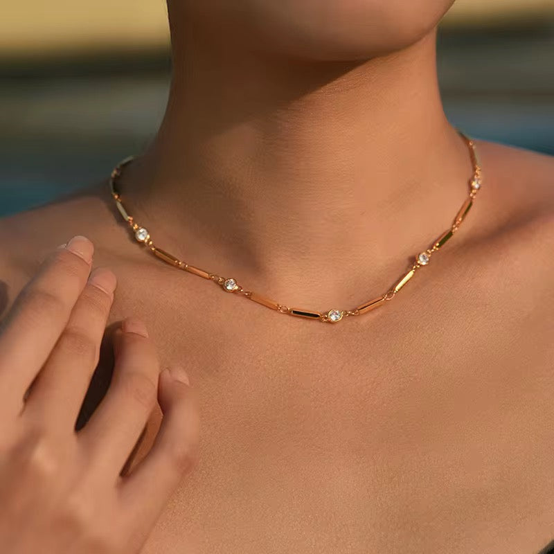 Gold necklace with small diamonds on a person's neck against a blurred natural background