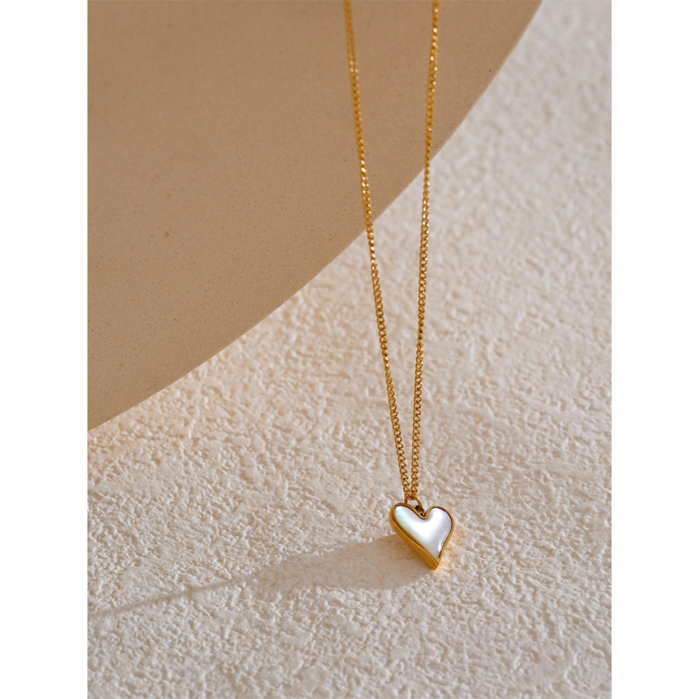 Gold necklace with a heart-shaped pendant on a textured beige surface