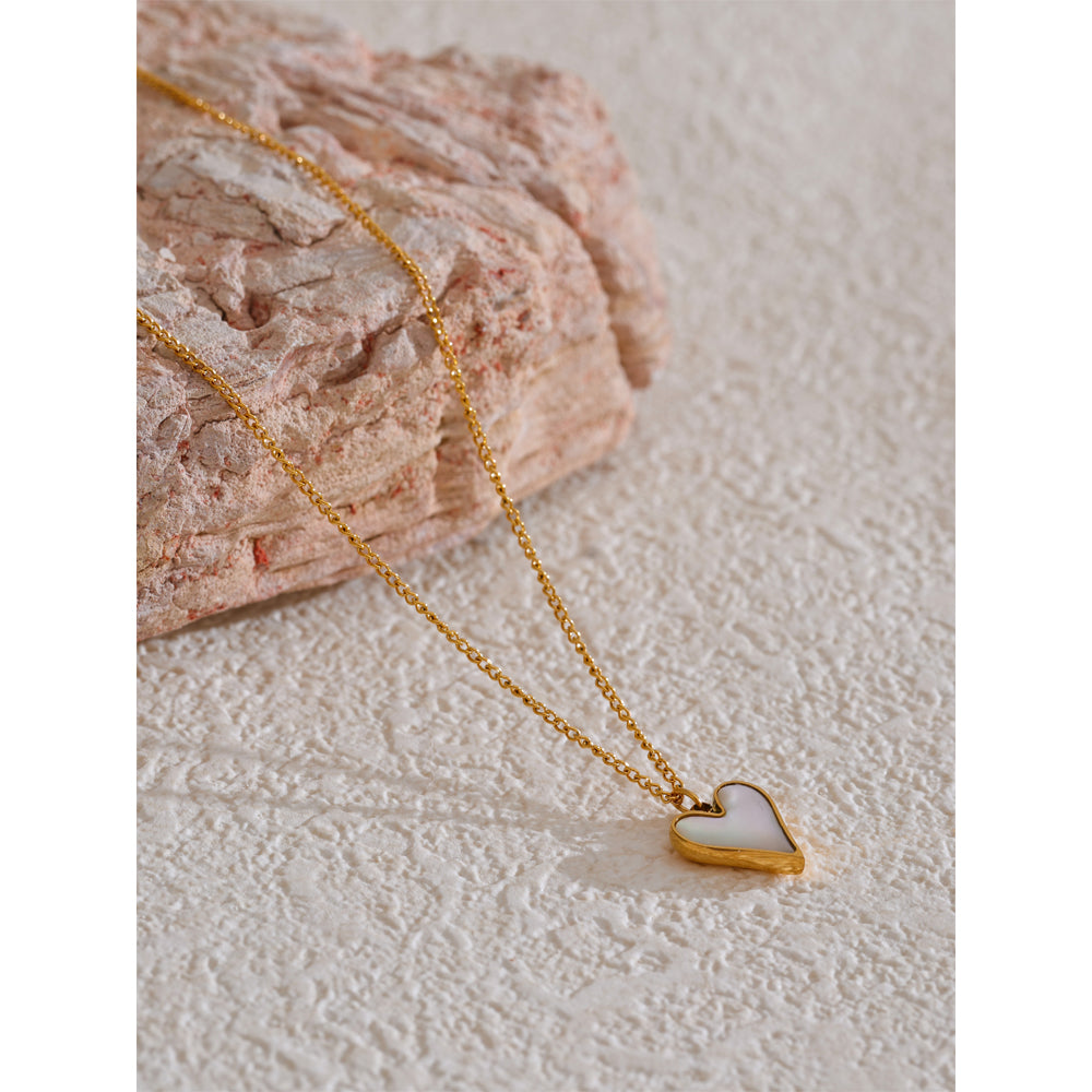 Gold necklace with a heart-shaped pendant on a textured surface