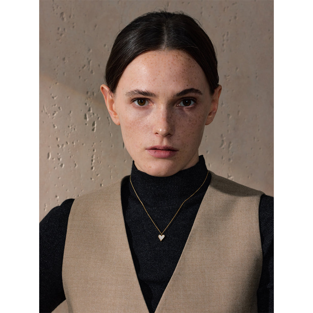 Woman wearing a beige vest over a black top with a neutral background