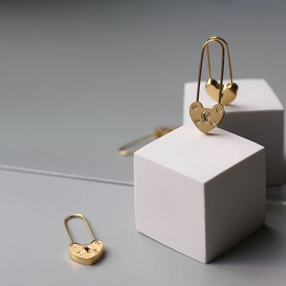Gold heart-shaped lock earrings on a gray background