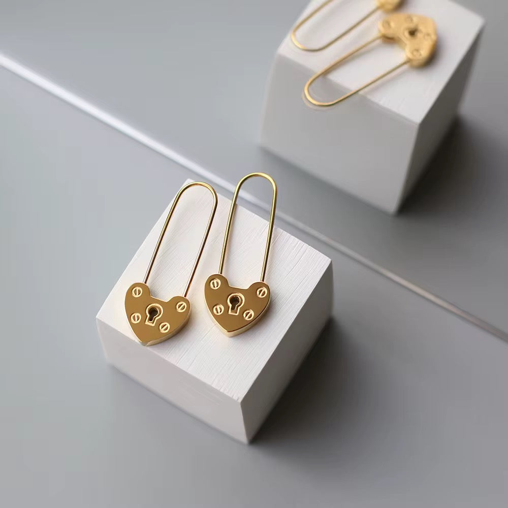 Gold heart-shaped lock earrings on a white stand with a gray background