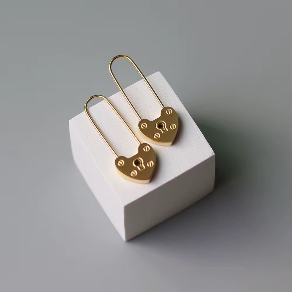 Gold heart-shaped earrings on a white stand with a gray background