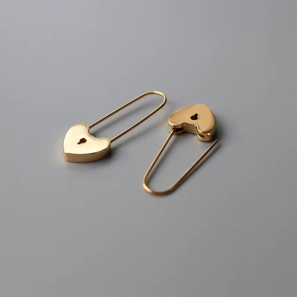 Gold heart-shaped safety pin earrings on a gray background