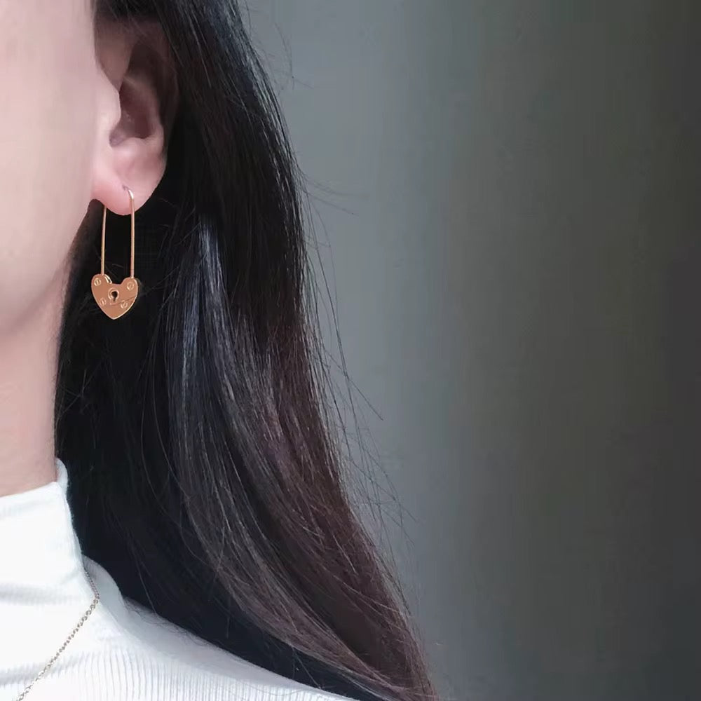 Heart-shaped earrings worn by a person with long dark hair against a gray background