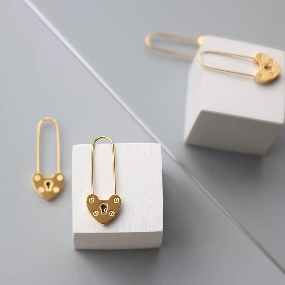 Gold heart-shaped earrings with lock design on a white cube against a light gray background