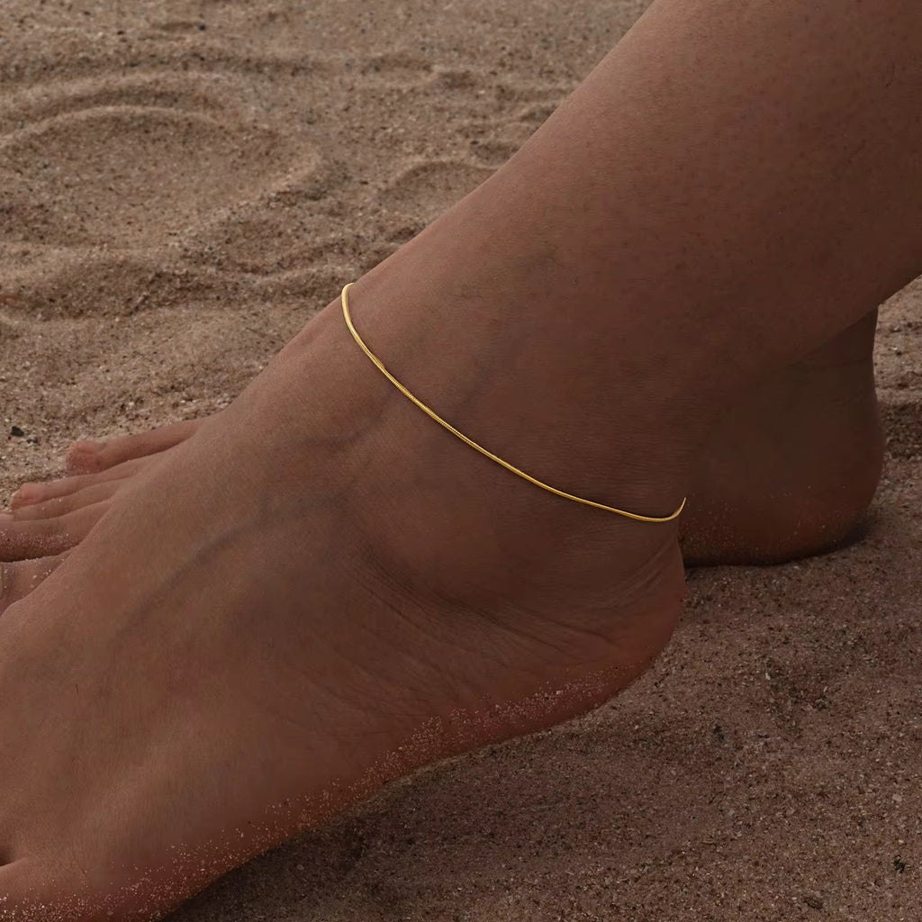 Gold anklet on a foot against a sandy background