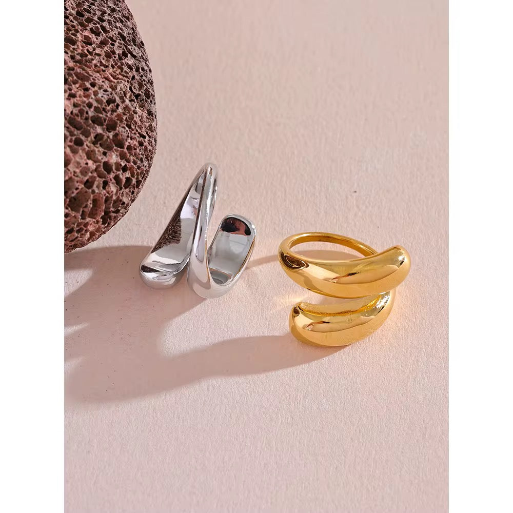 Two rings, one gold and one silver, on a textured beige surface.