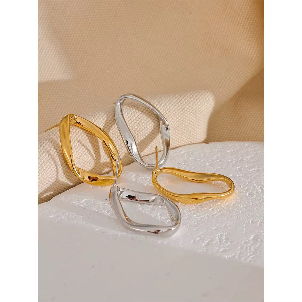 Pair of gold and silver hoop earrings on a textured surface with a beige fabric background.