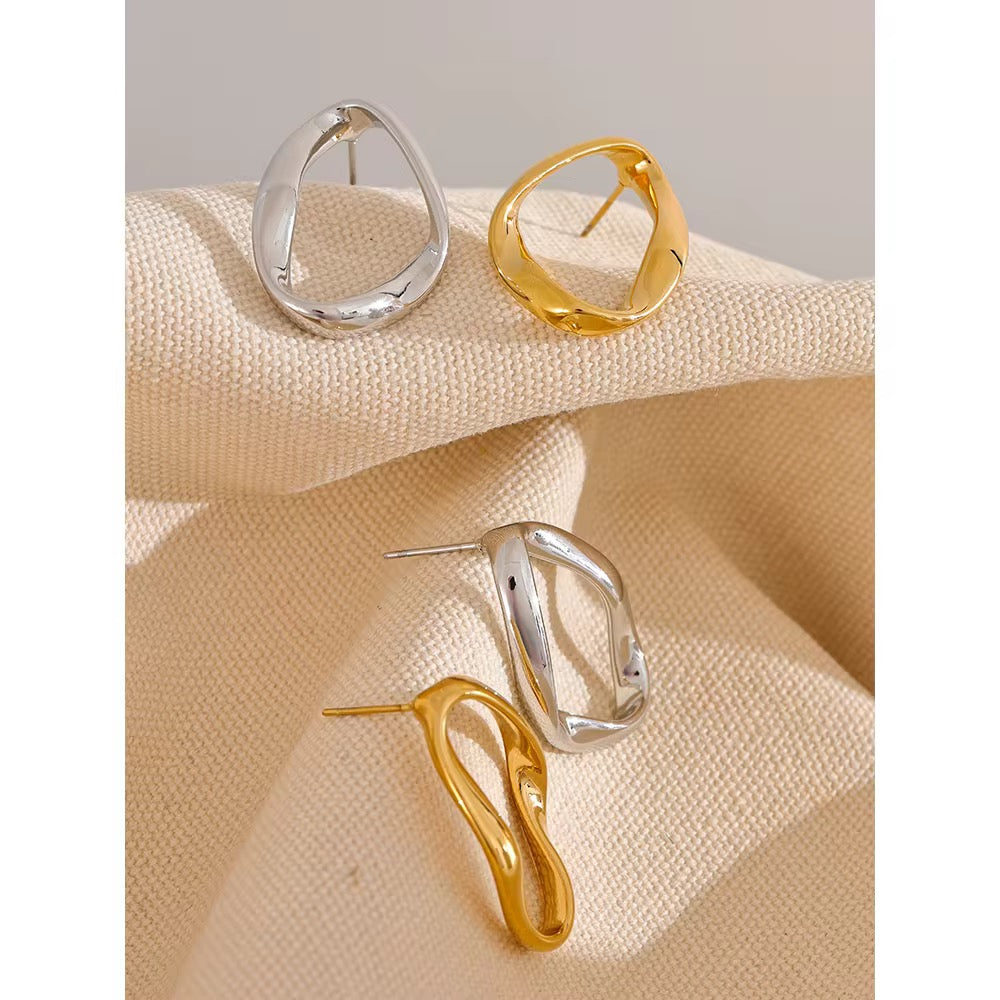 Gold and silver earrings on a textured beige surface with a gray background