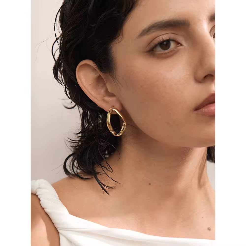 Close-up of a woman wearing gold hoop earrings with a neutral background