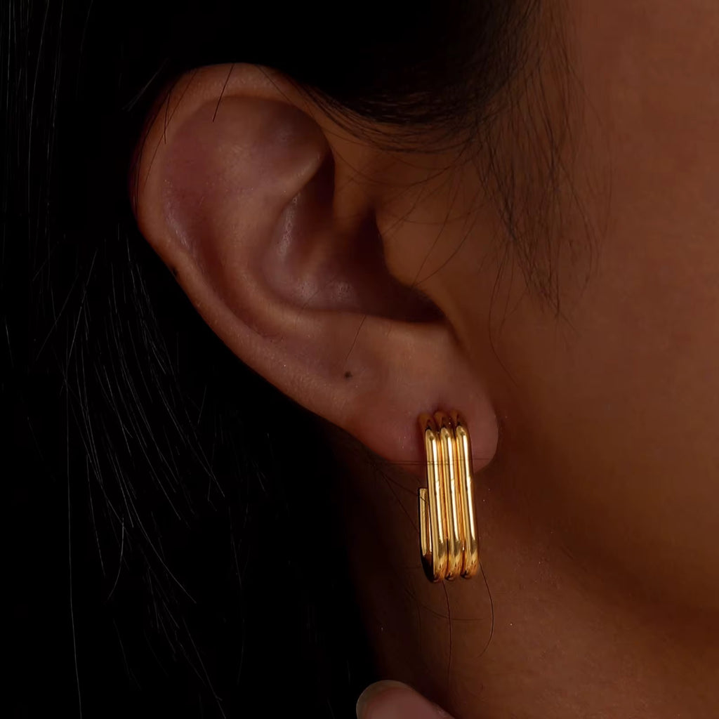 Gold hoop earrings worn by a person with a dark background