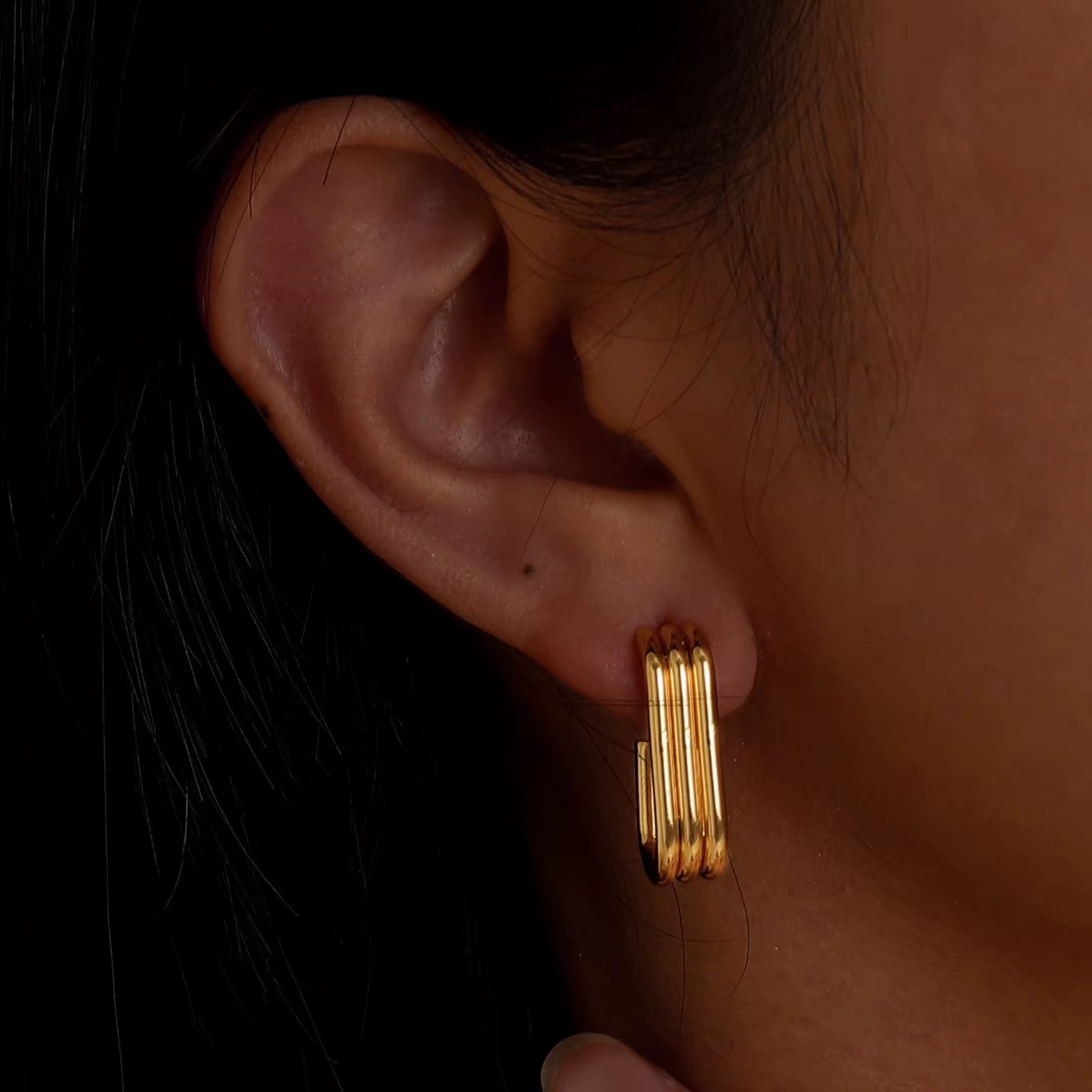 Gold hoop earrings worn by a person with a dark background